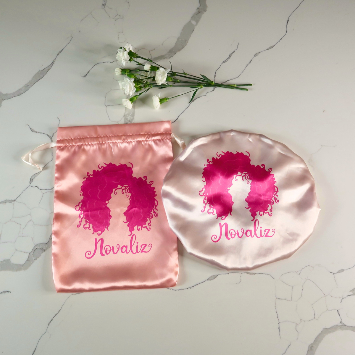 double layer satin bonnet in rose gold color, paired with the matching satin bag also in rose gold with a hot pink novaliz logo