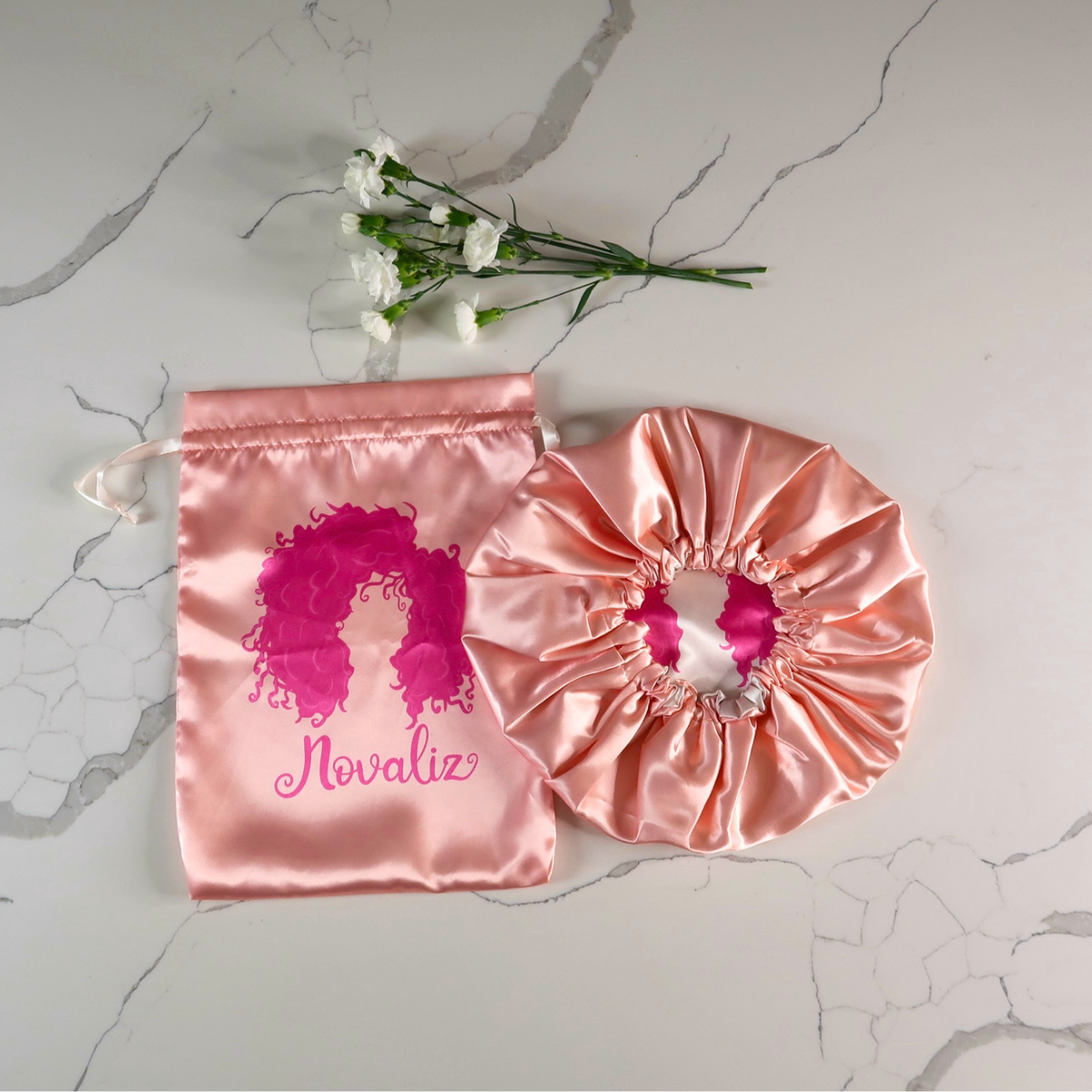 double layer satin bonnet in rose gold color, paired with the matching satin bag also in rose gold with a hot pink novaliz logo